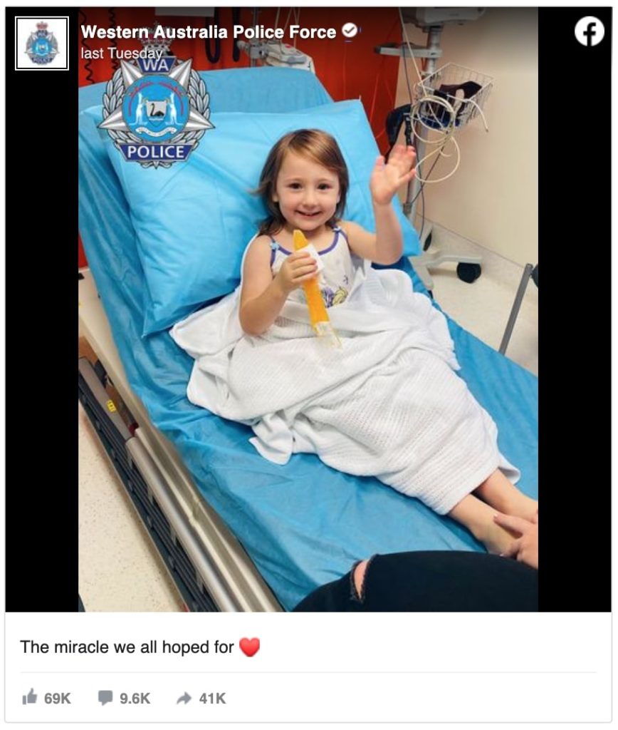 a smiling cleo waves from a hospital bed, icy pole in one hand